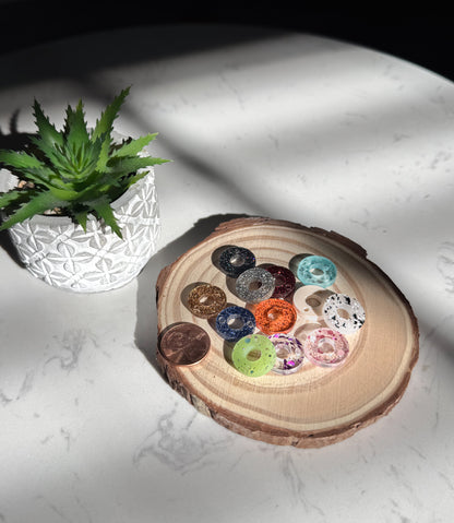 Colorful donut-shaped charms in a wooden holder on a white surface
