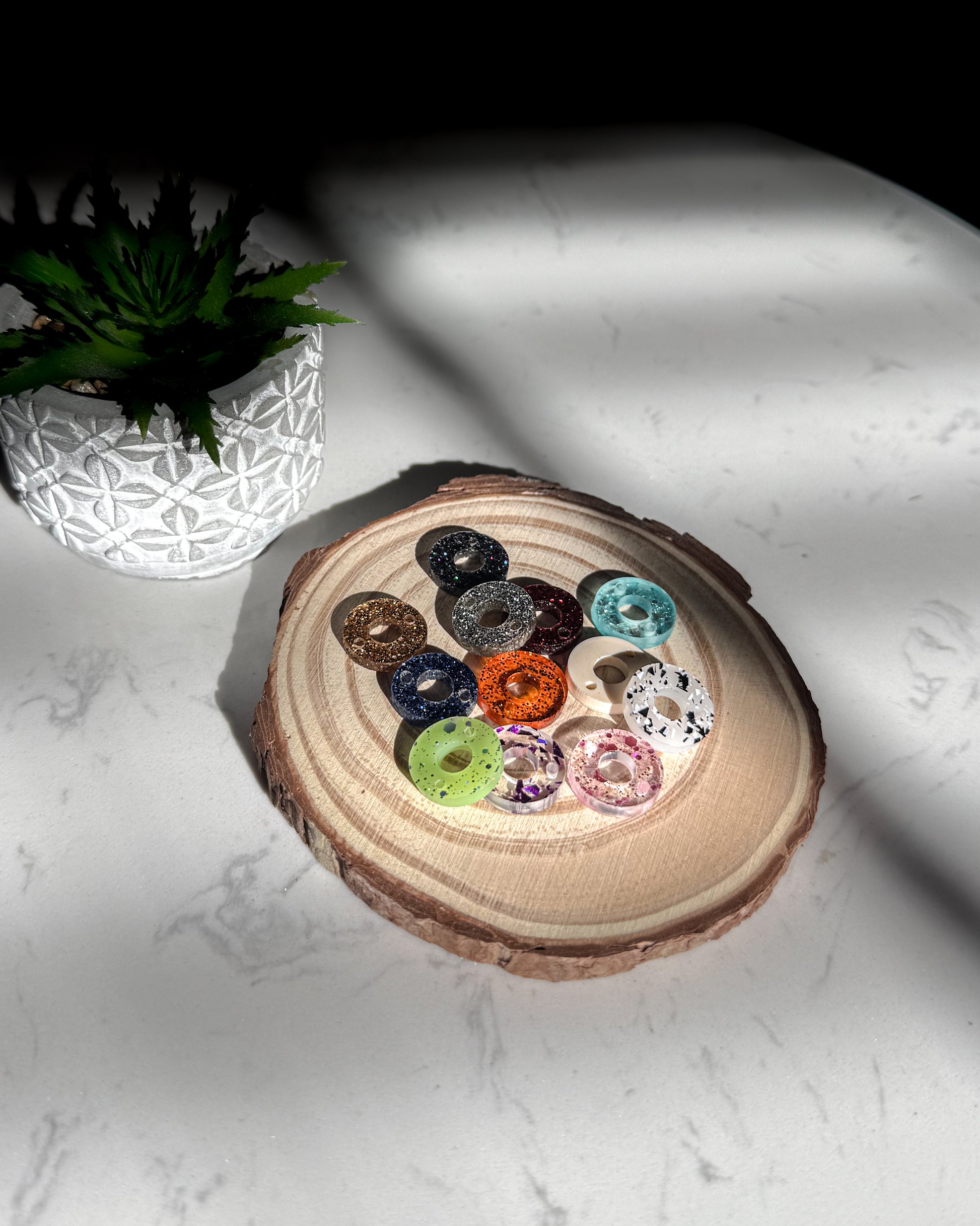 Colorful donut-shaped charms in a wooden holder on a white surface.