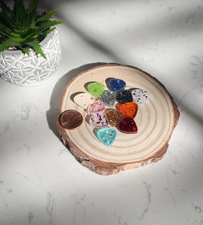 Colorful guitar pick-shaped charms in a wooden holder on a white surface